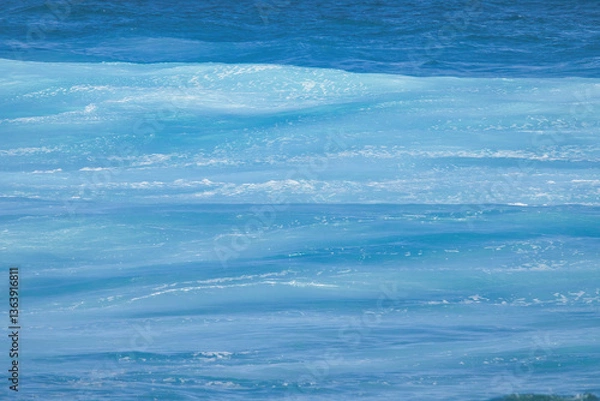 Fototapeta Many shades of blue of an ocean wave moving towards shore.