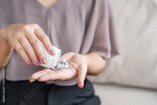 Obraz close up of woman's hand holding a bottle of medicine while taking vitamin pills or supplements such as probiotics, zinc, or magnesium to support her health and well being