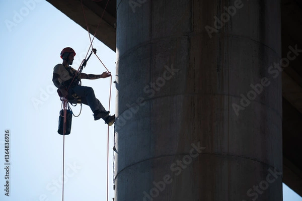 Fototapeta Rope access technician securing himself with a rope on concrete bridge pillar