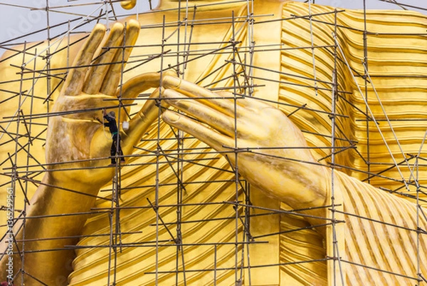 Fototapeta Painters are painting big golden Buddha statue under construction in Thai temple.