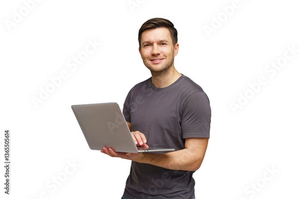 Fototapeta Young man smiling while holding a laptop and standing against a white background in a casual setting