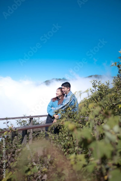 Fototapeta A couple is standing on a wooden bridge, looking out over a lush green forest