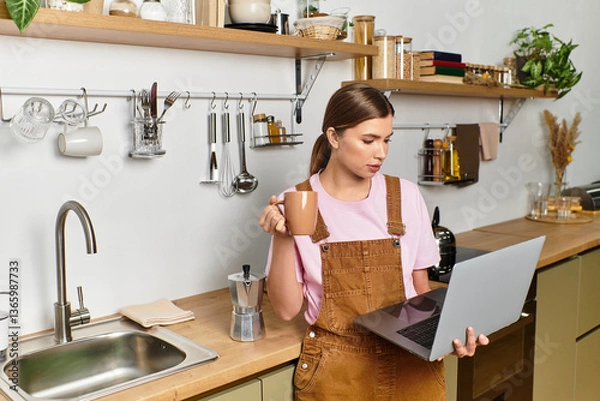 Fototapeta Enjoying a morning brew while working on a laptop in a cozy modern kitchen atmosphere
