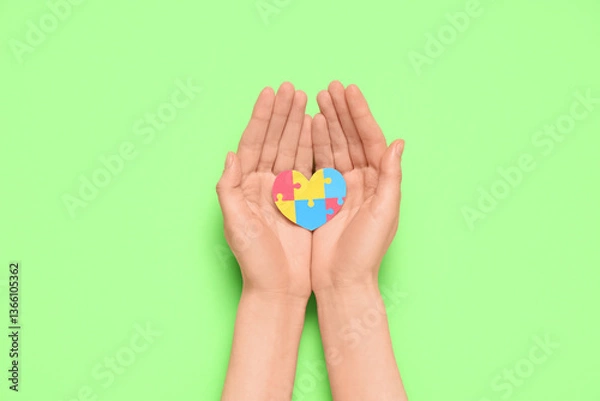 Fototapeta Female hands holding colorful puzzle pieces in shape of heart on green background. Autistic disorder concept
