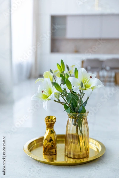 Obraz Bouquet of white artificial lilies in a golden vase on a table on a light background.