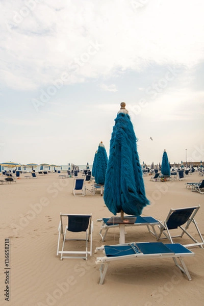 Fototapeta Deserted cold beach with umbrellas and sunbeds.