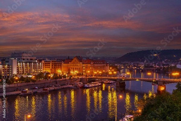 Fototapeta From an elevated vantage point, Prague, Czech Republic, reveals its enchanting beauty at night, showcasing the Vltava River, illuminated architecture along its banks, and a colorful sky at dusk.