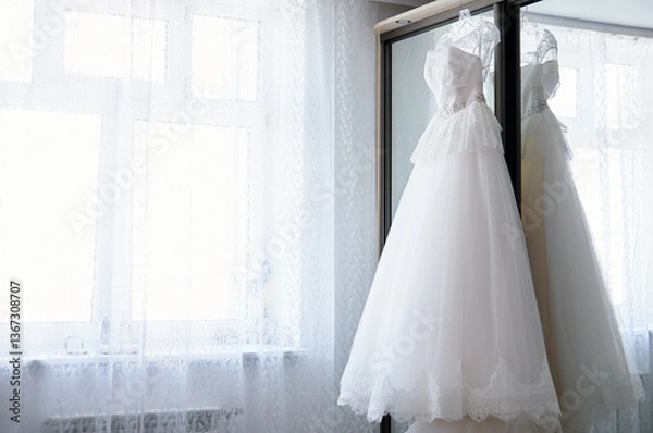 Obraz Elegant White Wedding Gown Hanging by a Mirror in Bright Daylight..