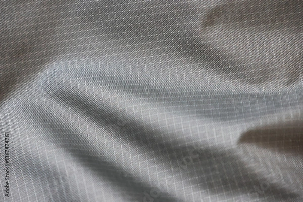 Fototapeta A close-up of a smooth, gray fabric with a tightly woven pattern. The material has a glossy finish and is likely used for outdoor gear such as jackets or backpacks due to its durability