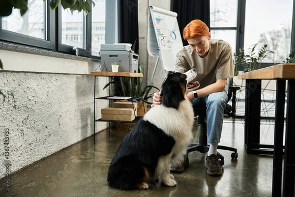 Obraz Young red haired man interacts with a friendly dog in a modern office environment