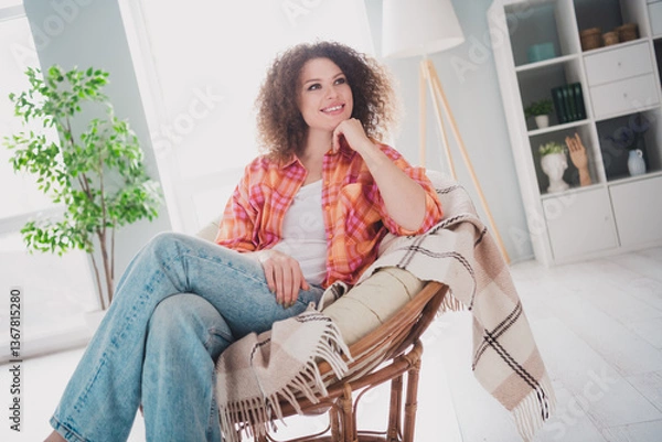 Fototapeta Attractive woman relaxing at home in a cozy living room, enjoying leisure time while sitting on a rattan chair