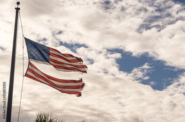 Obraz American flag torn down the middle waving in the wind on a cloudy sky. Resistance