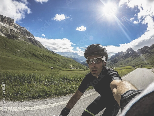 Obraz Corvara, Doloimites Italy. Young man on bicycle take a selfie in a beautiful landscape on Pass Pordoi.  Training on road bike on a mountainous road in a Dolomites.