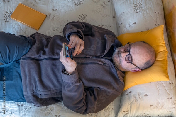 Fototapeta Man Relaxing on a Bed While Using a Smartphone