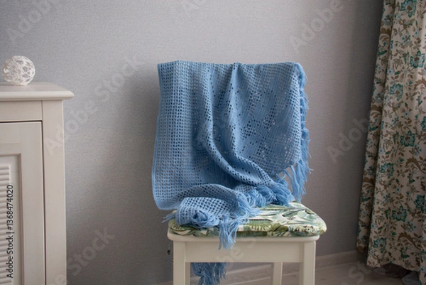 Fototapeta A blue shawl knitted using the fillet knitting technique hangs on a white chair