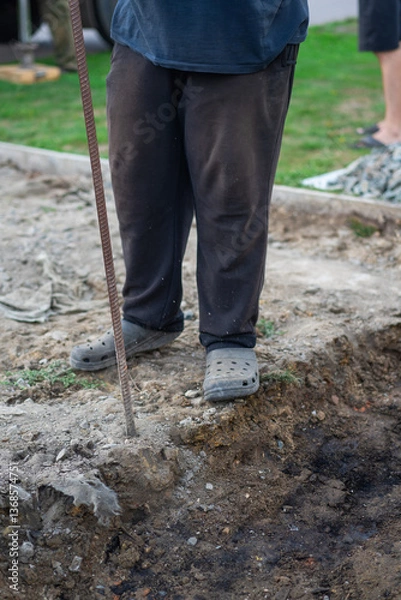 Fototapeta A man in old clothes is chiseling the ground with a crowbar