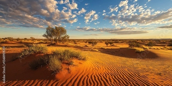 Fototapeta A serene desert landscape at sunset with rippling sand dunes and sparse vegetation.