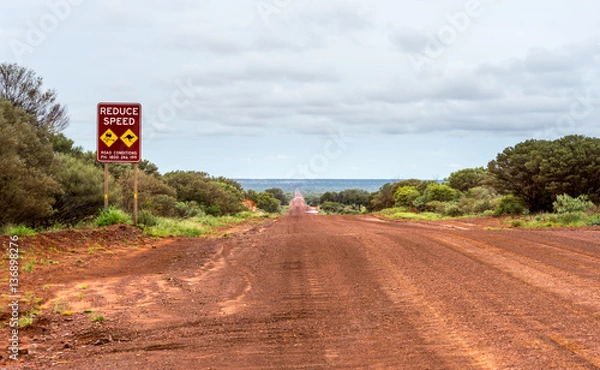 Obraz Outback Red Gravel Road. Red gravel road near Kings Canyon, NT Australia. Reduce speed sign with iconig kangaroo warning. Cloudy sky, red ocher soil.