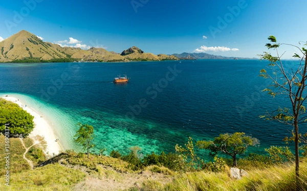 Fototapeta Komodo Coral Bay Viewpoint. View over white sand beach and coral bay at Komodo, Flores Indonesia. Grass in the foreground and mountains in the background.