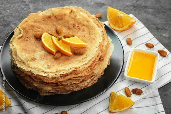 Fototapeta Stack of delicious pancakes with orange and nuts on black plate