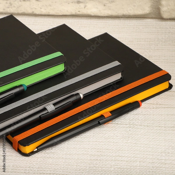 Fototapeta Black notebooks with colorful elastic bands and pens resting on textured surface