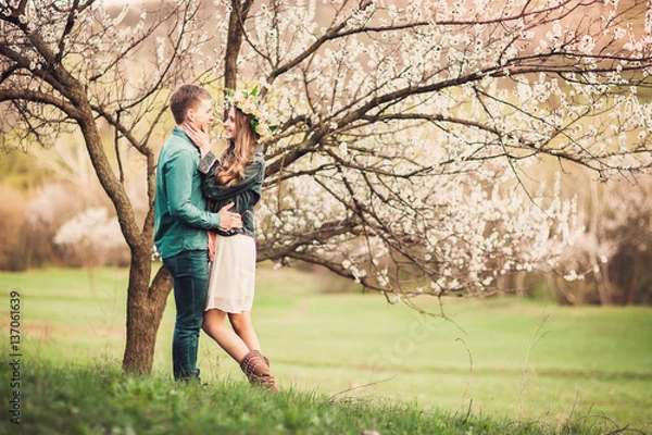 Obraz Młoda para zakochanych o randce pod drzewami różowy kwiat wiśni w czasie zachodu słońca. Miłość i czułość w okresie wiosennym
