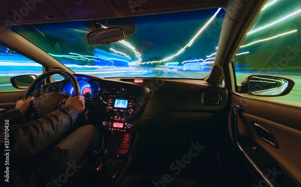 Fototapeta hands on the wheel a car moves at fast speed at the night. Blured road with lights with car on high speed