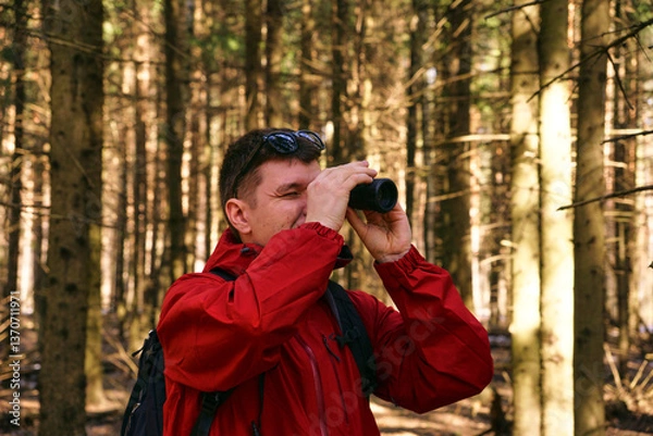 Fototapeta A man looks through monocular binoculars in the woods in nature. Search for new opportunities
