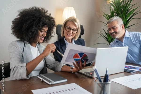 Fototapeta Three busy happy middle aged professional business man and two women executive leaders team using laptop working on computer at work desk having conversation on financial project at meeting in office.