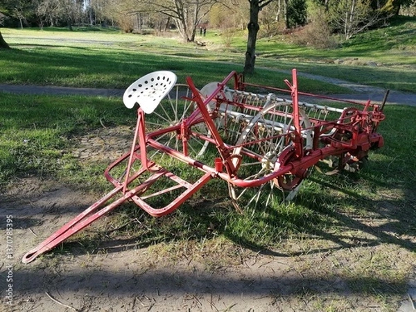 Obraz A rustic metal farming implement with a seat in front, likely an antique seed drill. The aged metal and unique design reflect traditional agricultural tools.