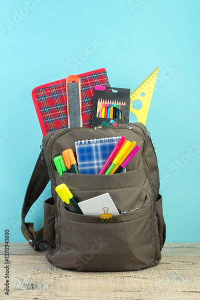 Obraz Backpack with different colorful stationery on table. Light blue background. Back to school.
