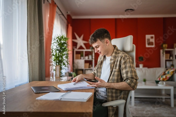 Fototapeta young man student study for exam from notes and mobile phone at home