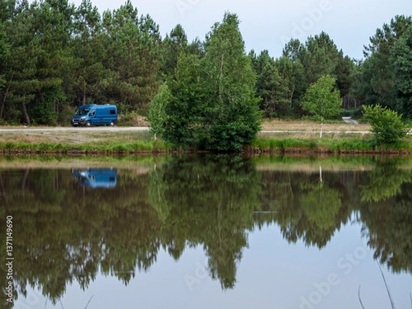 Obraz Vistas de una furgoneta azul reflejada en el Étang du Petit Broustier  en Laruscade, Francia. Con paisaje verde de árboles, en Francia verano de 2022