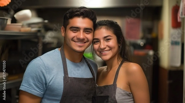 Obraz Happy young couple in casual clothing posing in kitchen with aprons and smiling warmly