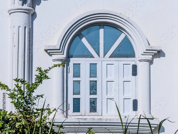 Fototapeta An arched window in a white classical building surrounded by greenery