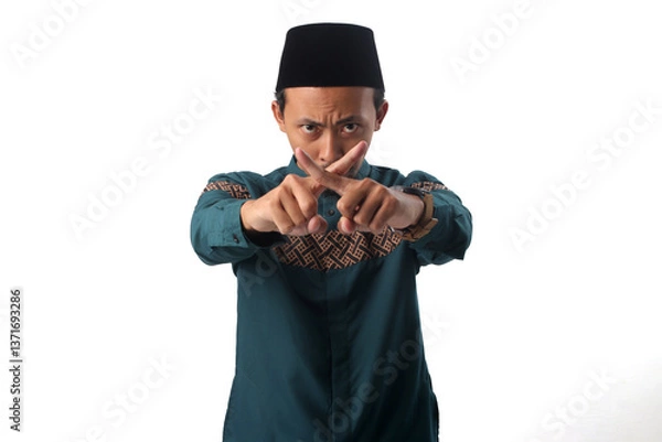 Fototapeta Asian Muslim man frowning with a serious expression, crossing his index fingers in an "X" gesture to signal prohibition, stopping forbidden actions during Ramadan fasting. Isolated on white background
