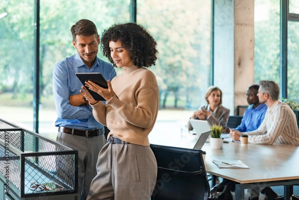 Obraz Two business people discussing work together using a tablet in a modern office