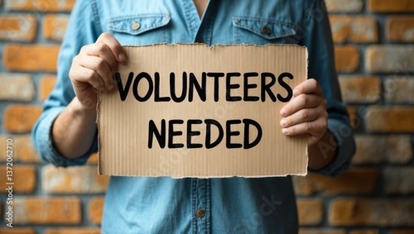 Obraz Man holding a cardboard sign with the words "Volunteers Needed"