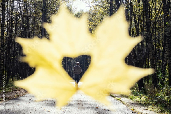 Fototapeta Breaking up couple. concept. Man going away in autumn park through a hole in the form of heart of maple autumn leaf in a woman hand.