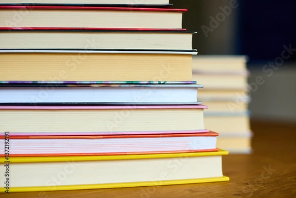 Fototapeta A collection of colorful books stacked neatly on a wooden table, evoking a sense of warmth and inviting readers to explore the stories within them.