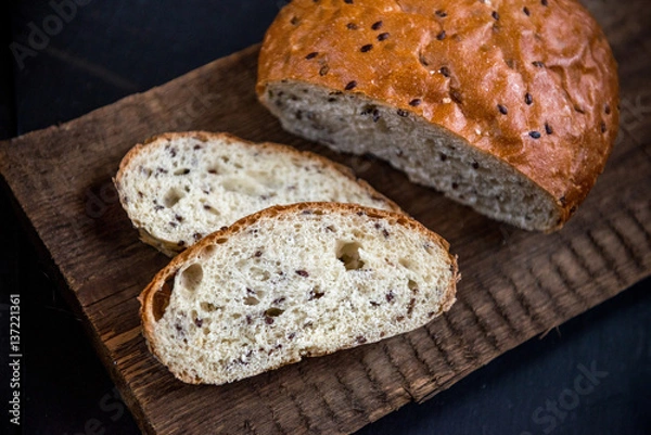Fototapeta The whole grain bread with flax seeds, on slate and wooden background.