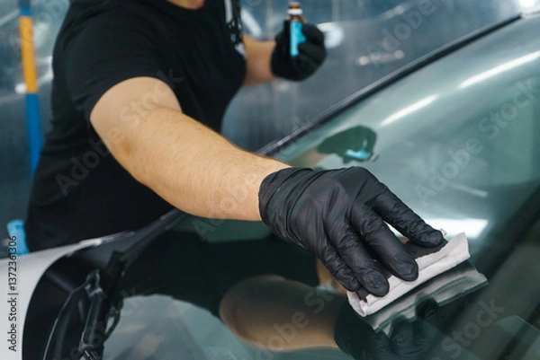 Fototapeta A master in black gloves applies a nano protective coating to a car windshield.