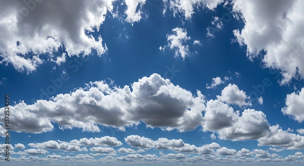 Fototapeta Capture the vast sky with fluffy white clouds dynamically against a bright blue background,