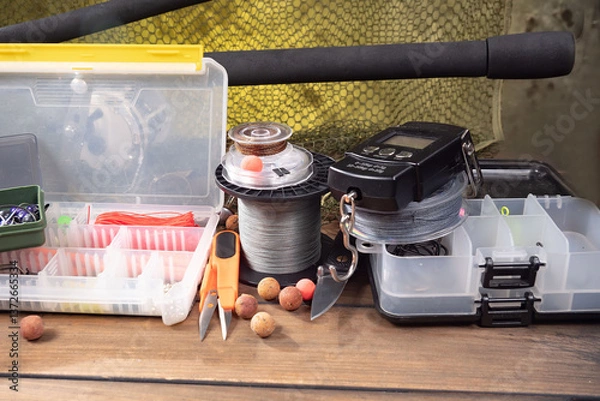Fototapeta Sport fishing equipment on a table in a studio in a composition, against a wooden background and a fishing net.