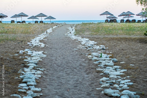 Obraz A rock marked road down to beach. There are sunshades and sunbeds and far away small horizontal area, sea is visible. Photo is taken in Antalya, Turkey