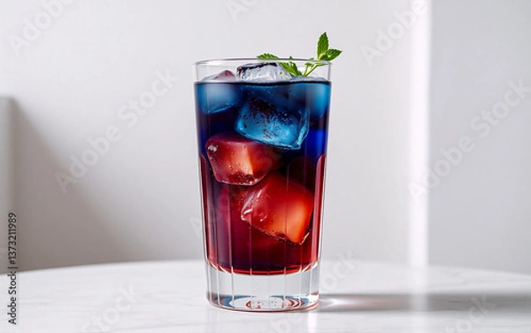 Fototapeta Tall glass filled with a vibrant layered drink, showcasing red and blue hues, chilled with ice cubes and garnished with a sprig of mint.