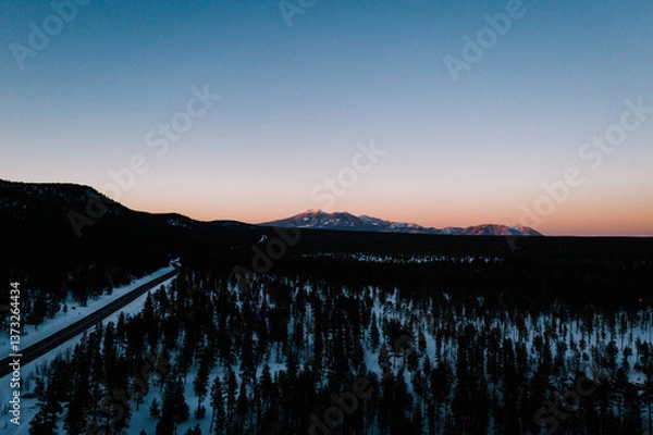 Fototapeta aerial view of a sunset over the mountains and snowy forest