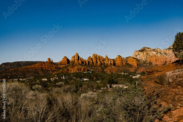 Fototapeta sun hitting red rocks in the background with trees and houses in foreground