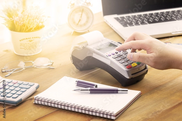 Fototapeta Cashier hand holding a Credit card over EDC machine or credit card terminal with calculator and glasses.