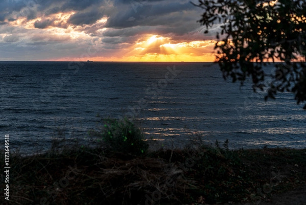 Obraz Gelendzhik resort. The sky is cloudy and the sun is setting. The sun is shining through the clouds, creating a beautiful orange and pink sky. The ocean is calm and the horizon is visible
